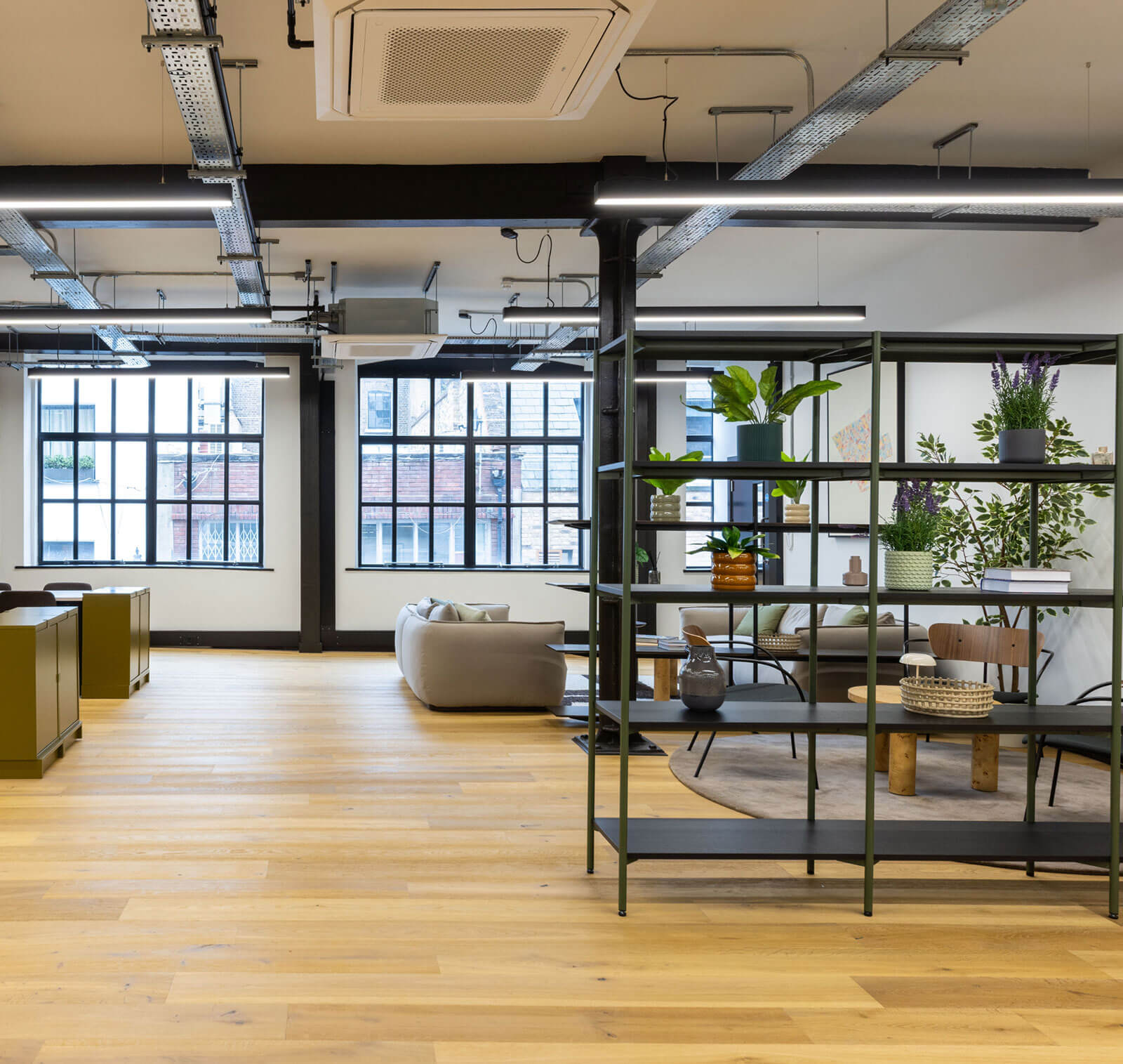 Open-plan warehouse-style office with exposed steelwork, large windows and plant-filled shelving