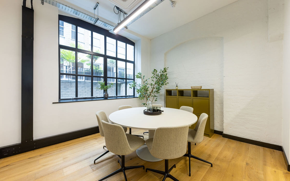 Small meeting room with a round table, upholstered chairs and a Crittall-style window