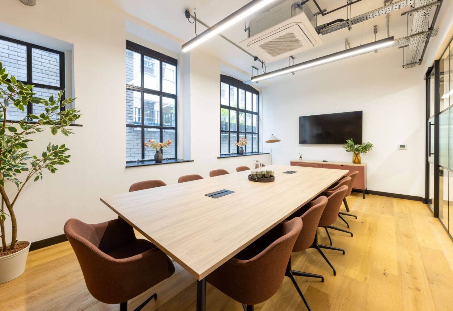 Boardroom with a long wooden table, rust-coloured chairs and a wall-mounted screen